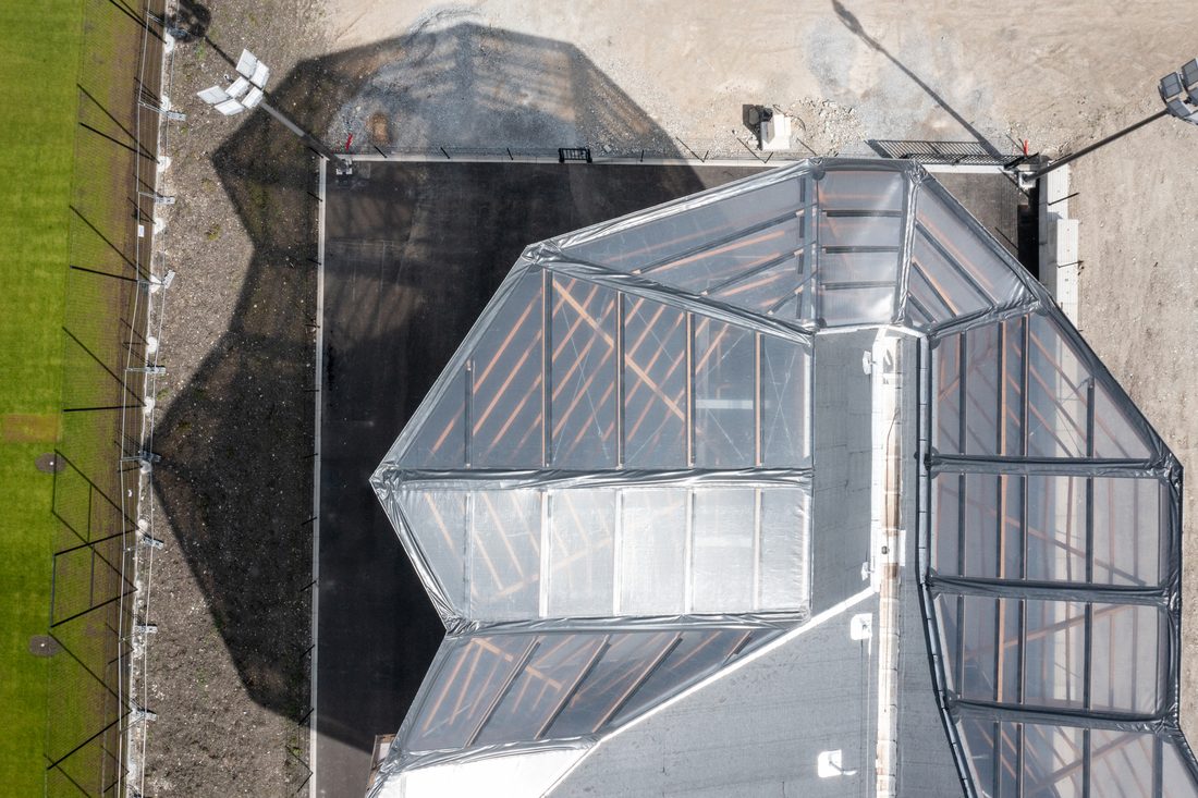 Aerial top view of a transparent canopy covering an outdoor climbing wall, showing its faceted geometric roof design.