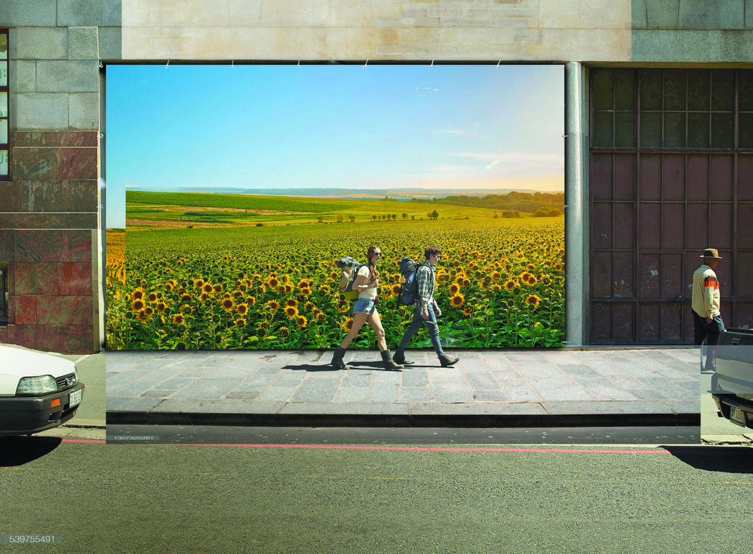 Grande bâche publicitaire imprimée représentant un champ de tournesols installée sur une façade urbaine, avec des passants marchant devant.