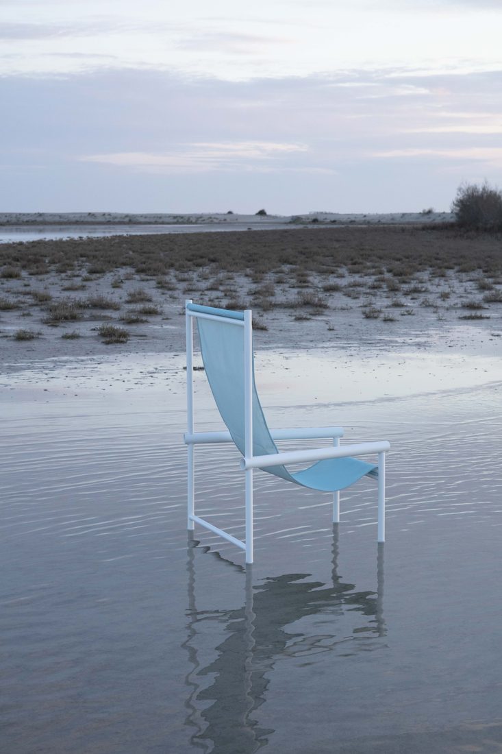 Chaise design en toile technique bleue, installée dans une zone d’eau calme au paysage minimaliste.