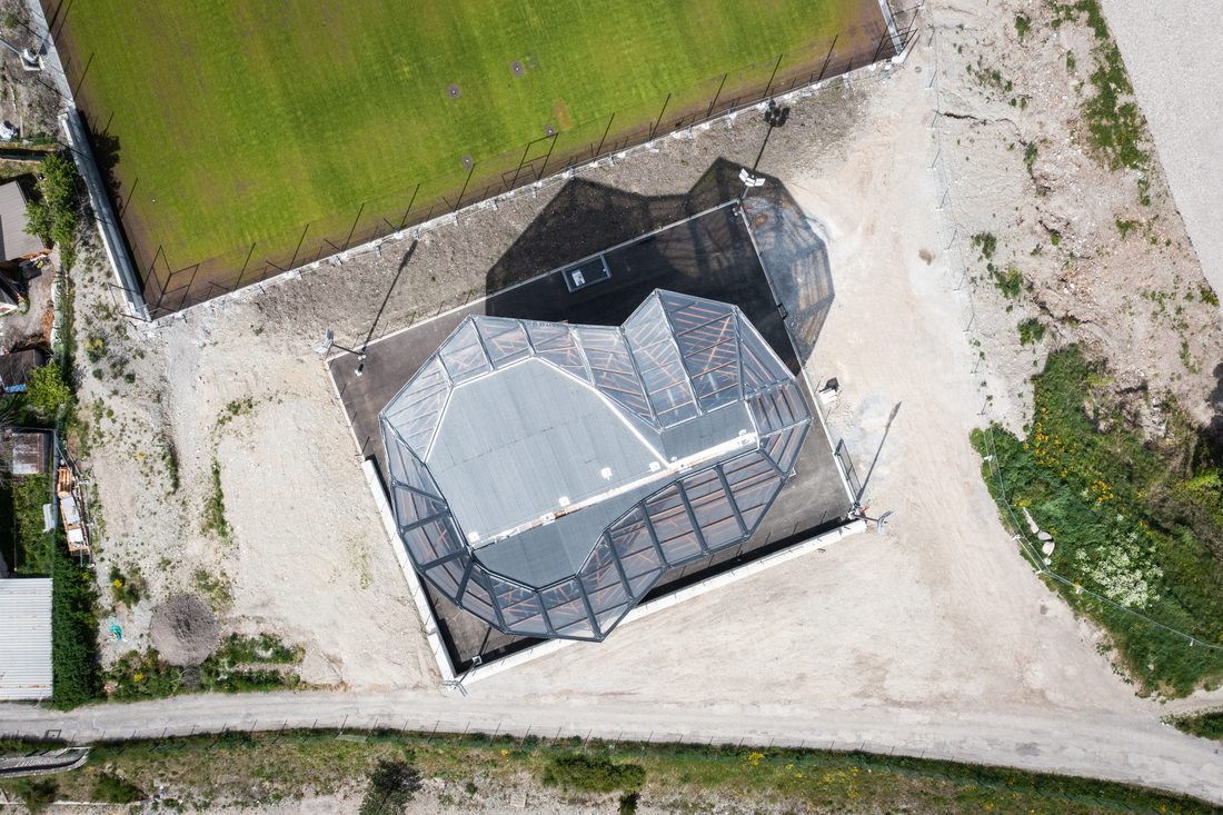 Top-down aerial view of an outdoor climbing wall installation with a transparent protective canopy in a sports complex.