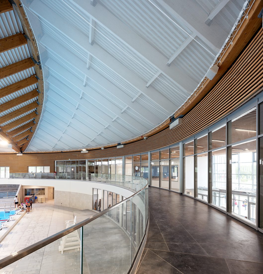Curved roof structure with skylights and timber beams overlooking the swimming pools at Taverny Aquatic Center