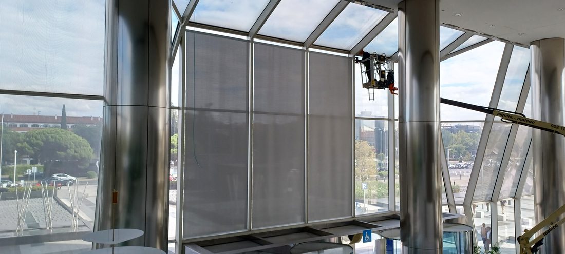 Stores enrouleurs techniques installés derrière une façade vitrée d'un immeuble de bureaux.
