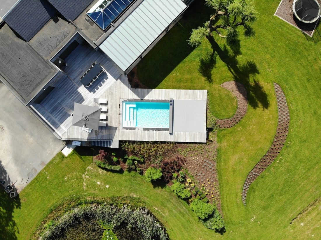 Vue aérienne d’une maison contemporaine avec piscine rectangulaire, couverture automatique et jardin paysager