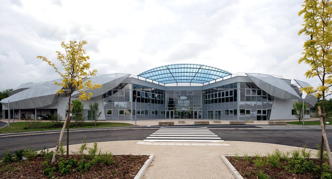 Upper-level walkway inside Aquatic Center of Taverny facing the curved roof and glazed façade