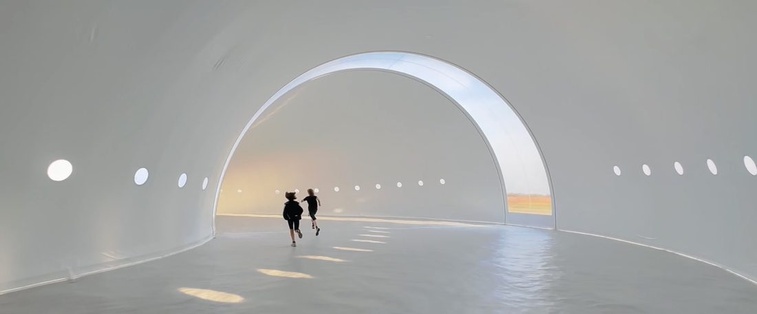 Intérieur d’une structure textile blanche en forme de voûte avec ouverture circulaire zénithale.