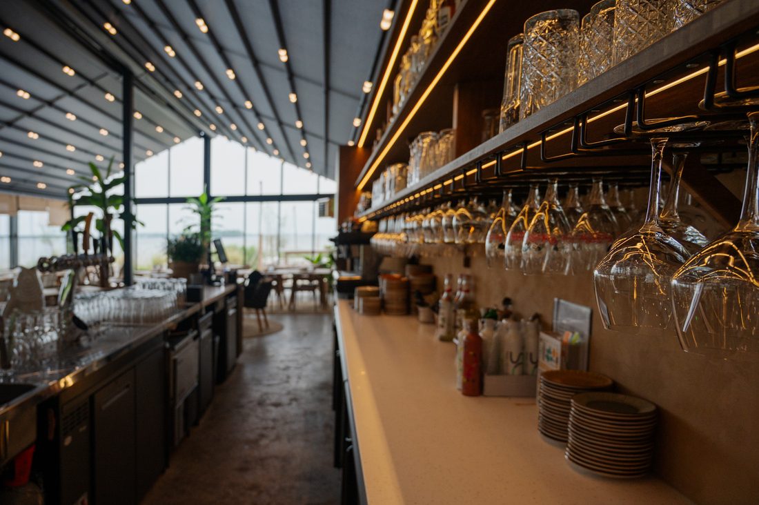 Restaurant bar counter under Soltis 96 Proof roof with suspended glass racks and warm lighting
