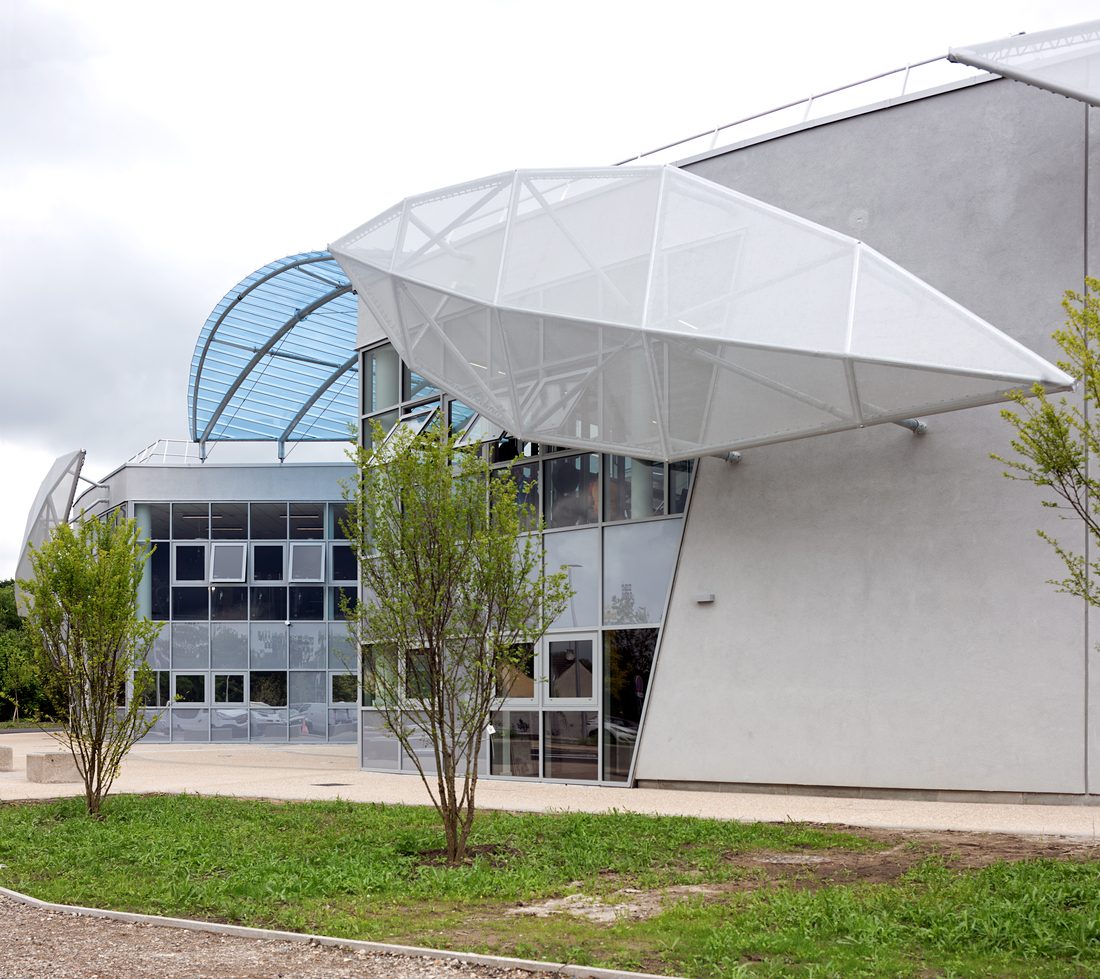 Side elevation of Taverny Aquatic Center with architectural textile façade under dramatic sky