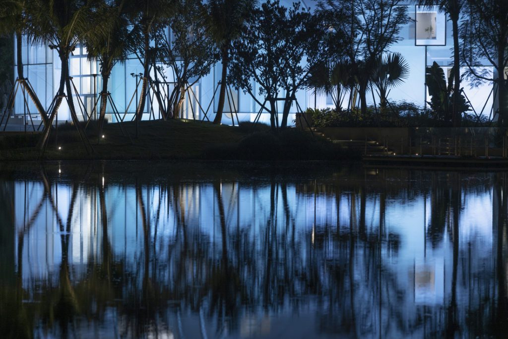 Façade en membrane composite translucide rétroéclairée, reflet sur un plan d’eau au premier plan.
