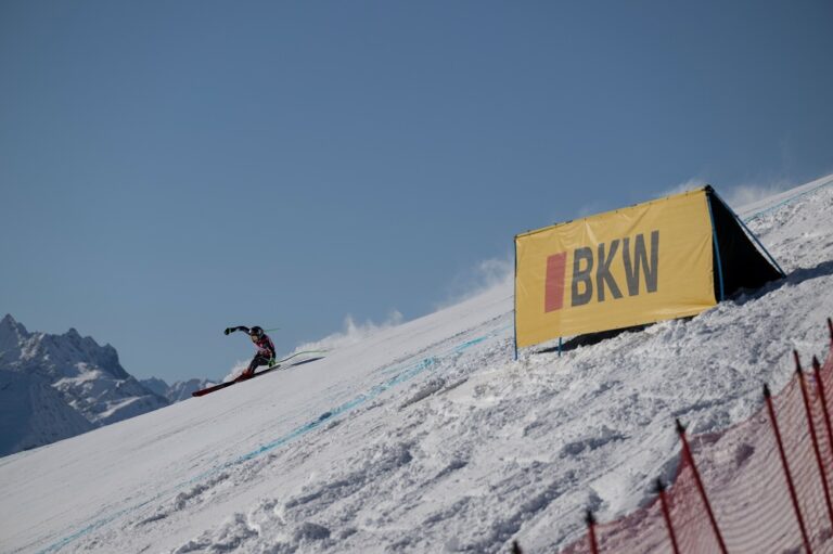 Skieur en pleine descente lors de la Coupe du Monde de ski alpin avec structure publicitaire BKW en textile technique Serge Ferrari