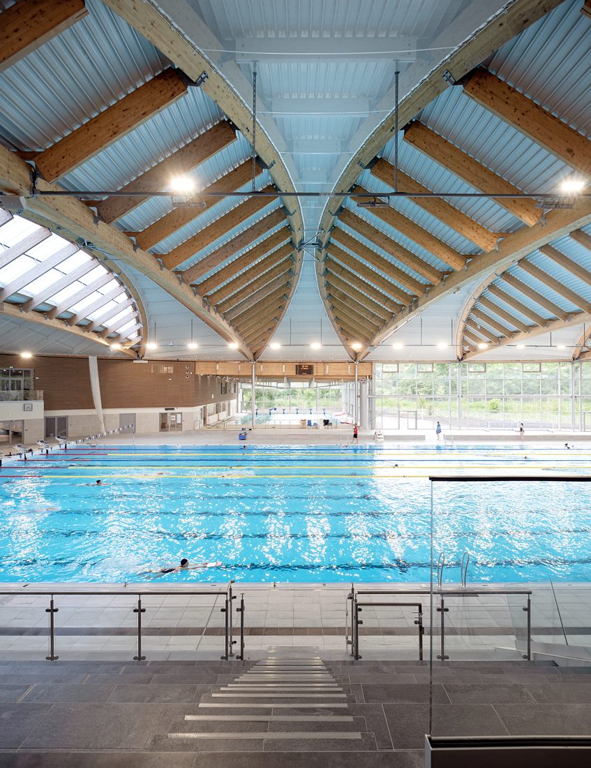 Diving pool area inside Taverny Aquatic Center with curved skylight roof and laminated timber structure