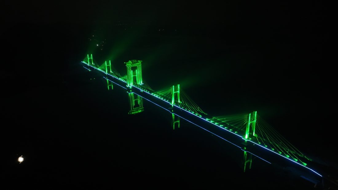 Ambhora Bridge illuminé de nuit avec éclairage LED vert et reflets sur l’eau.