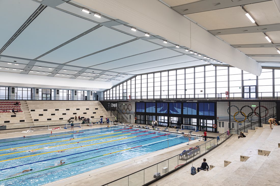 Bassin de natation intérieur avec plafond textile et larges façades vitrées.