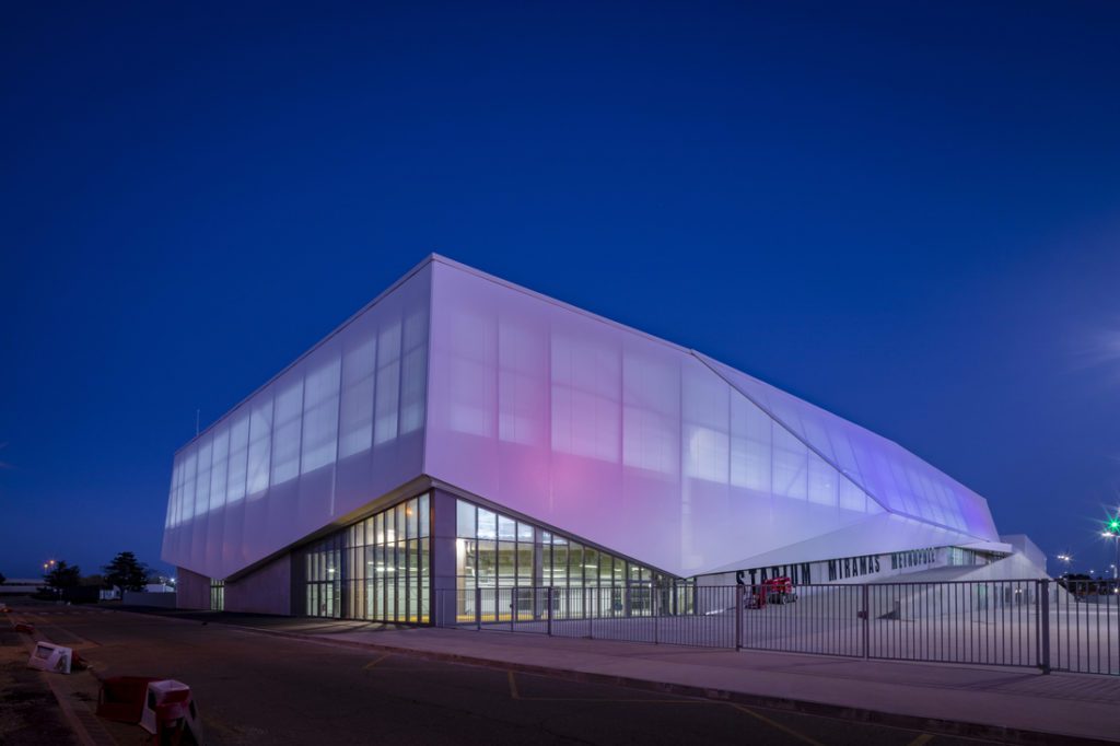 Façade de stade en membrane composite translucide, rétroéclairée, formant un volume architectural lumineux de nuit.