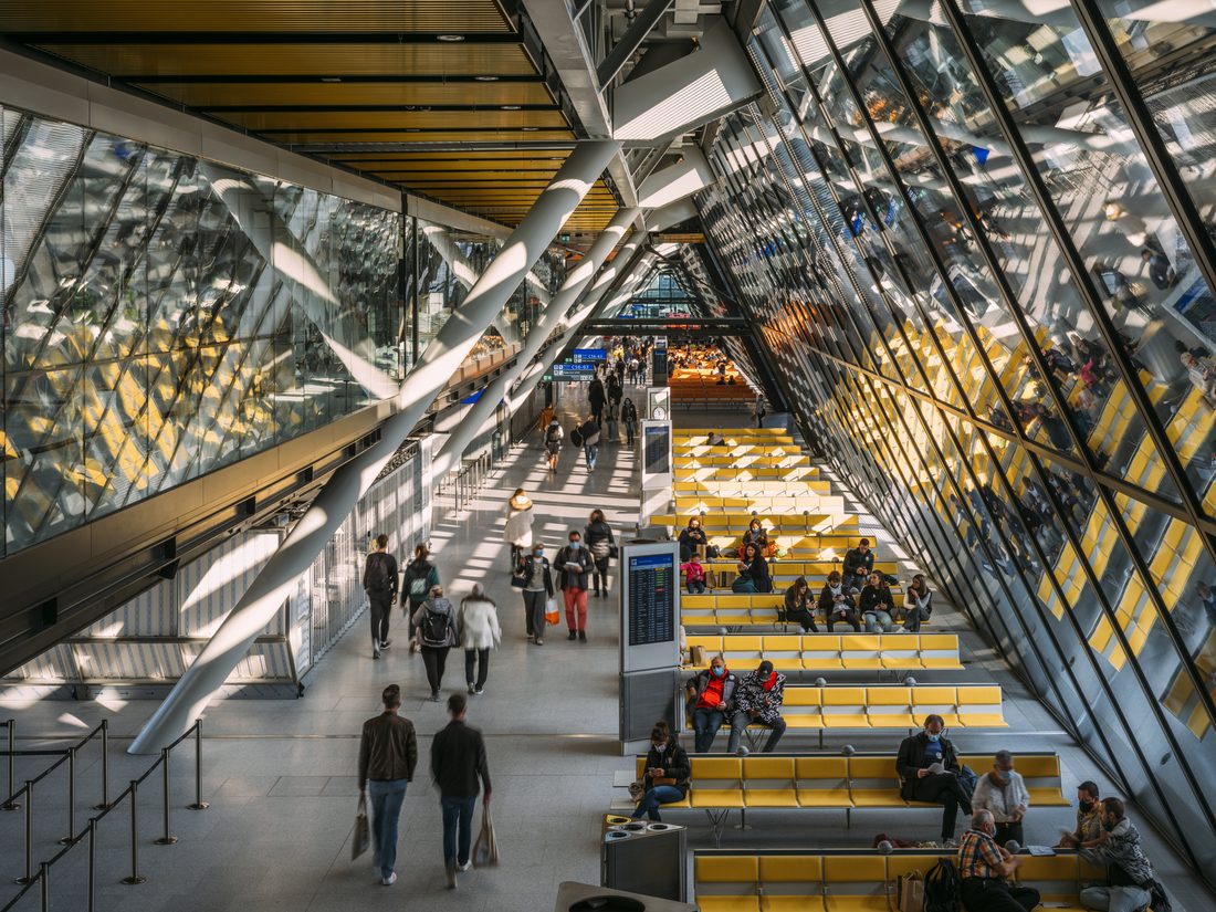 Zone d’attente d’aéroport avec assises jaunes et passagers dans un terminal lumineux à architecture vitrée.