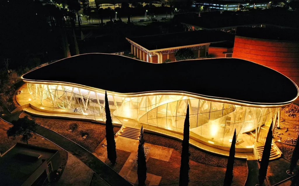 Aerial night view of the museum with a glowing curved façade clad in custom-printed Tenseo Frontside 381 textile mesh.