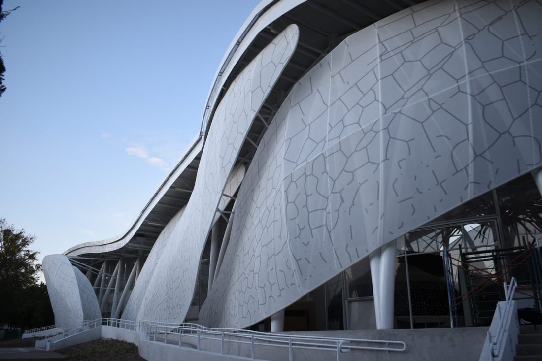 Curved museum façade clad in custom-printed Tenseo Frontside 381 textile mesh, showing wing-like panels and the exterior walkway.