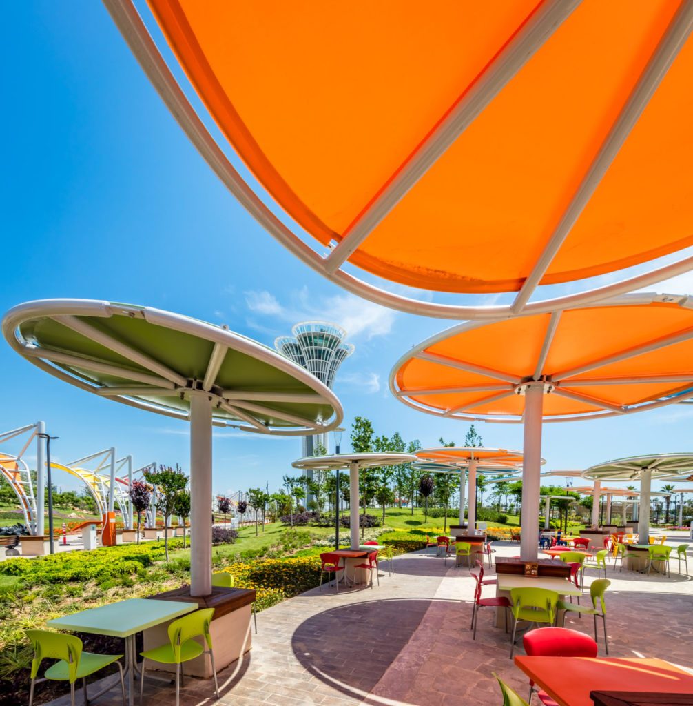 Ombrières circulaires orange et vert sur une terrasse extérieure avec tables et chaises