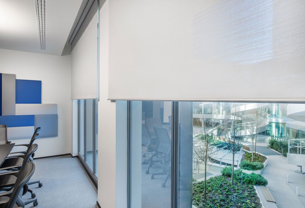 Détail de stores intérieurs Soltis Touch Bridge 3 installés devant une façade vitrée de bureaux.