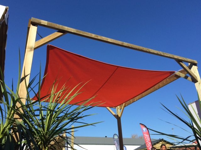 Voile d’ombrage rouge tendue sur une structure en bois sous ciel bleu