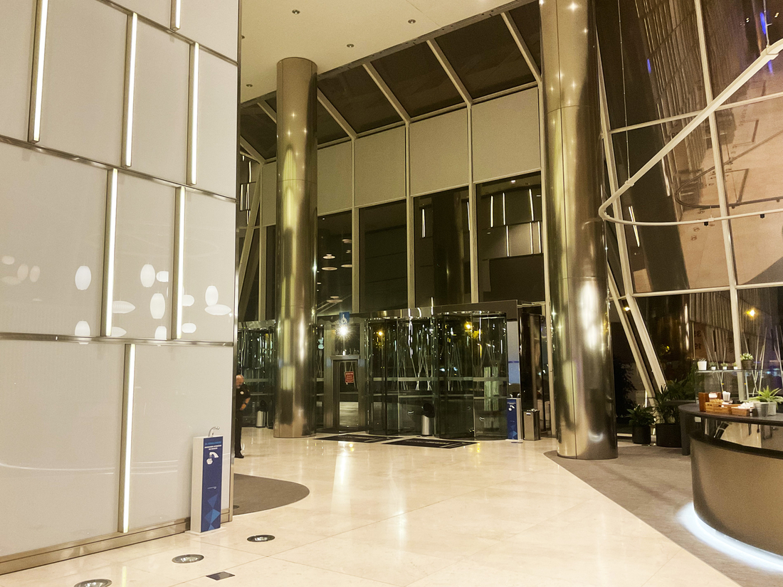 Hall vitré d'un immeuble tertiaire avec stores enrouleurs fermés en soirée.