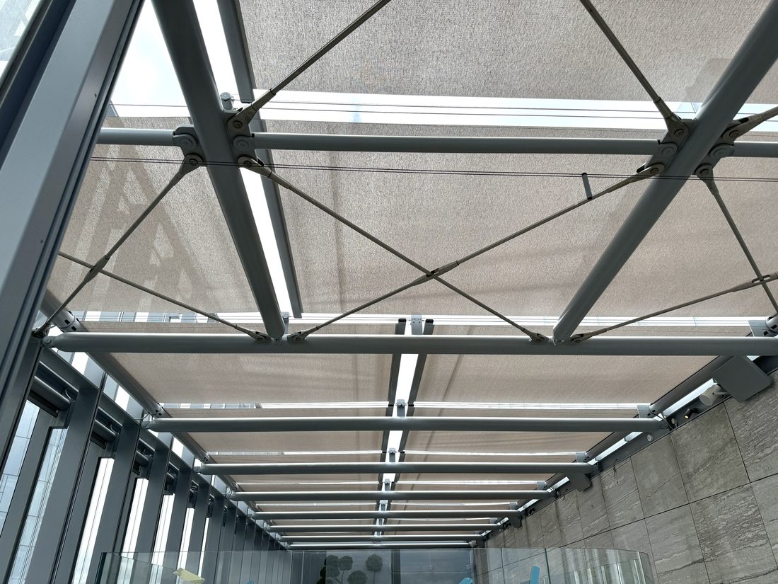 Système de toiture avec toiles de protection solaire Serge Ferrari installées sur une structure métallique pour filtrer la lumière naturelle.