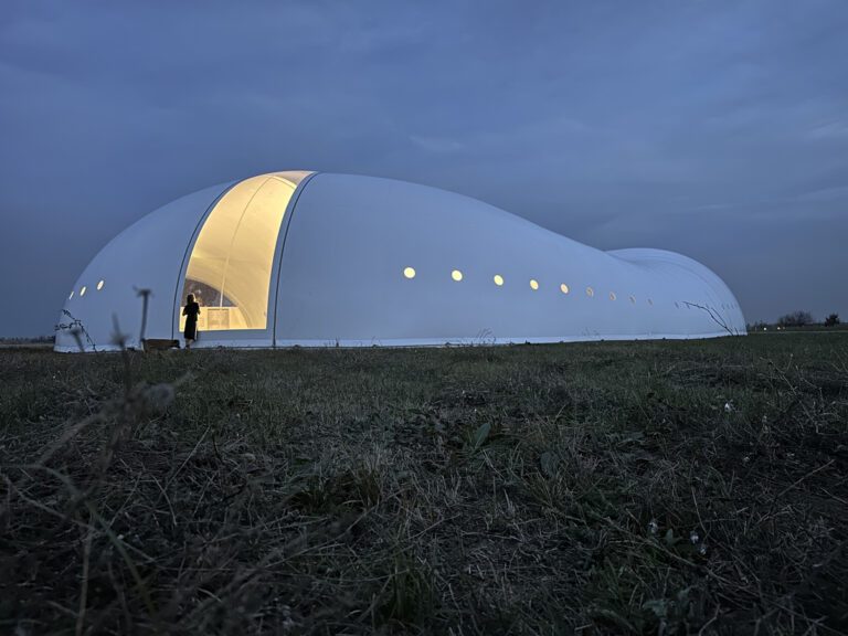 Façade latérale d’un pavillon textile blanc avec hublots circulaires.