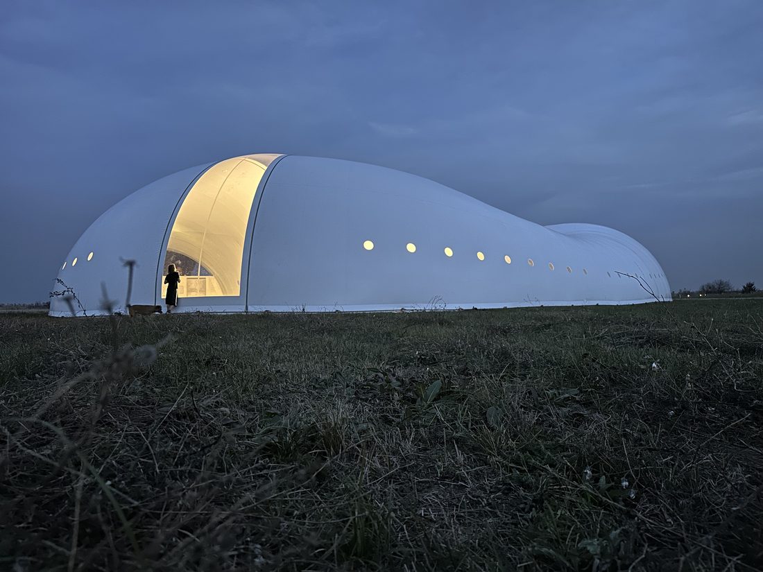 Façade latérale d’un pavillon textile blanc avec hublots circulaires.