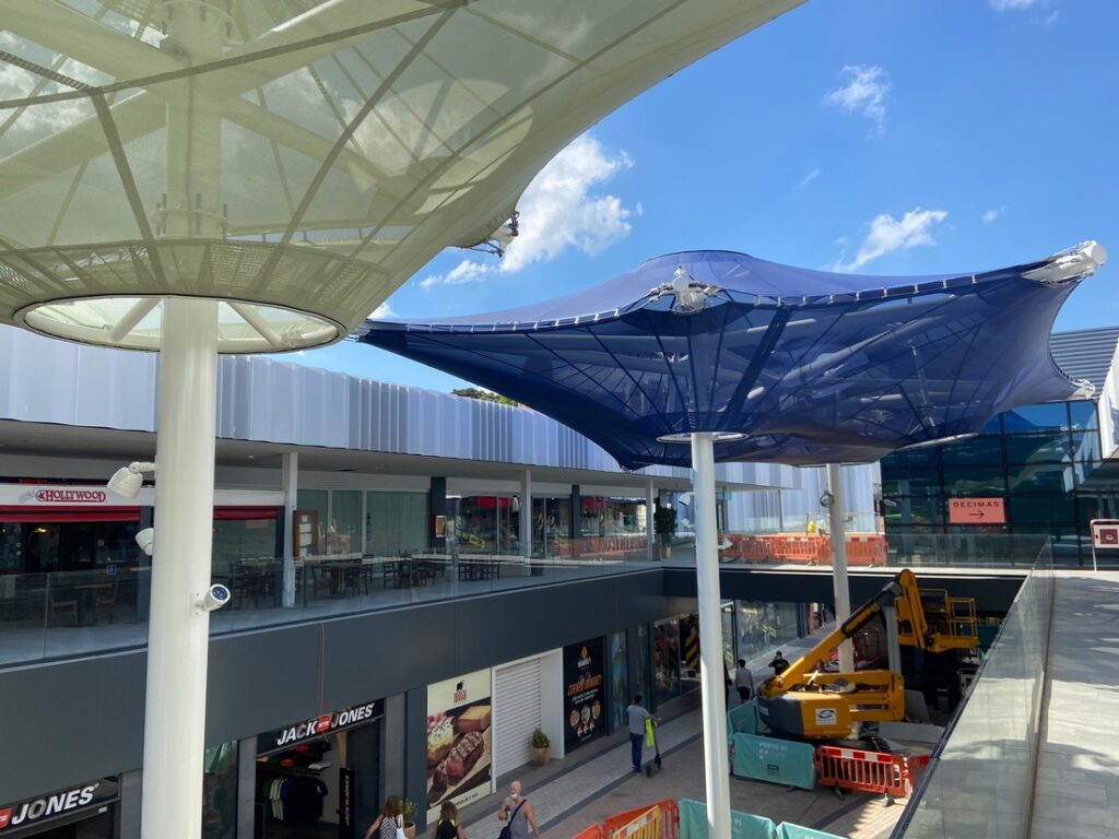 Voiles d'ombrage textiles installées au-dessus des terrasses et circulations d'un centre commercial.
