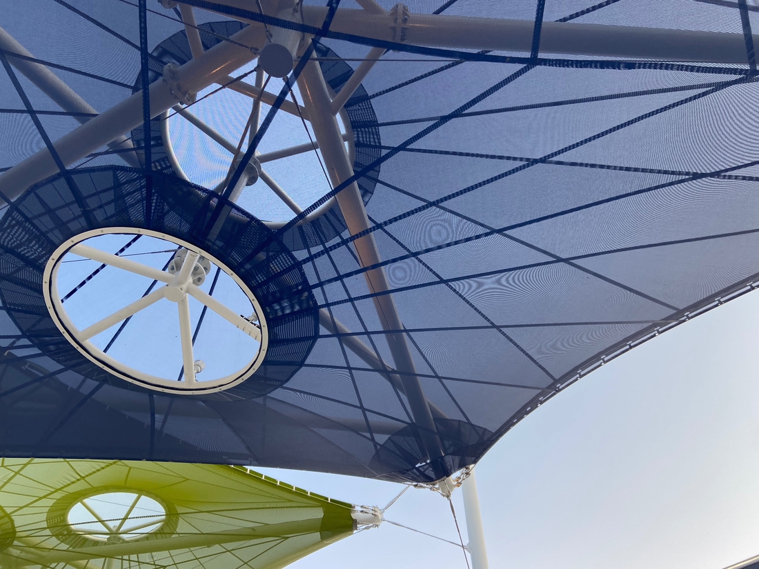 Détail d'une voile textile bleue avec ses câbles et anneaux de fixation.