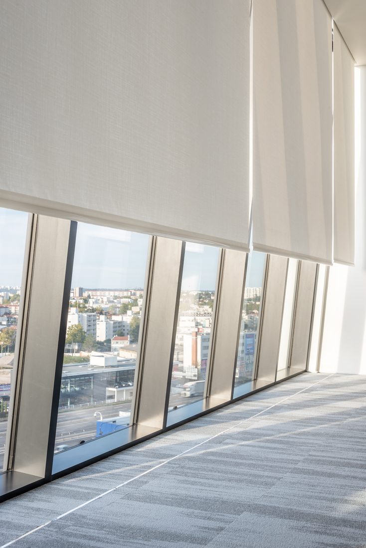 Stores enrouleurs intérieurs en toile filtrante sur façade vitrée inclinée