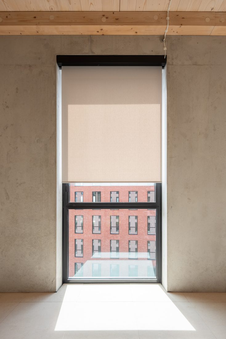 Fenêtre avec store enrouleur en membrane composite souple Serge Ferrari, filtrant la lumière naturelle pour un confort visuel optimal.