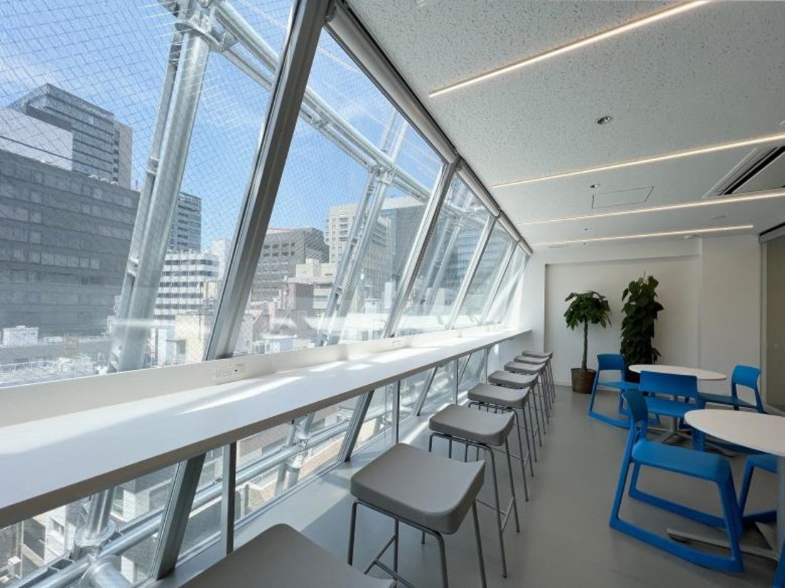 Interior lounge with large inclined windows and Serge Ferrari mesh façade overlooking Tokyo’s skyline.