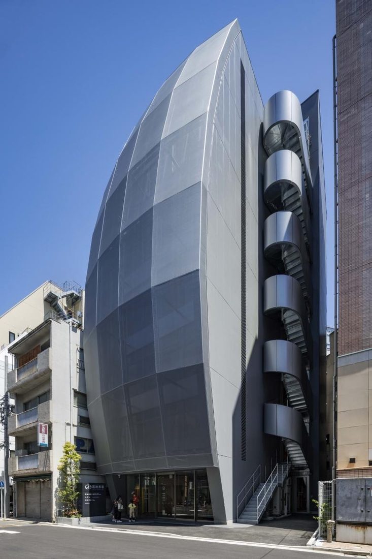 Daytime exterior view of the Building of Music in Tokyo with curved Serge Ferrari mesh façade and external staircase.
