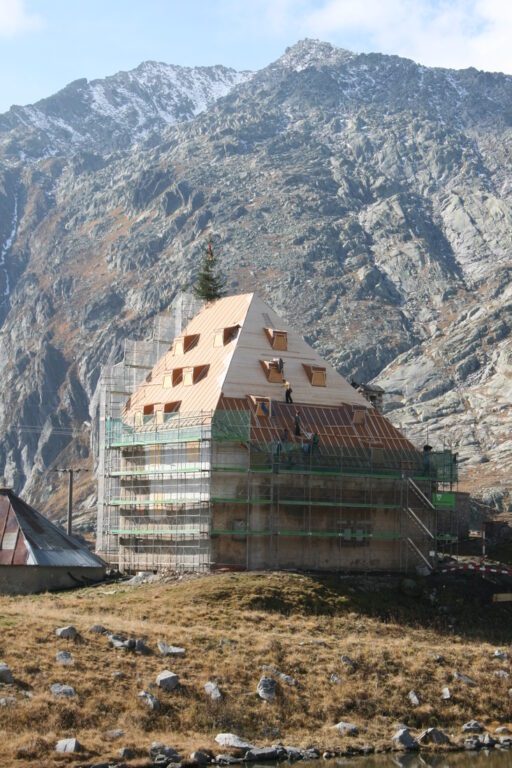 Bâtiment en rénovation sur un site de montagne, avec échafaudages et toiture en cours de construction, sur fond de massif rocheux.