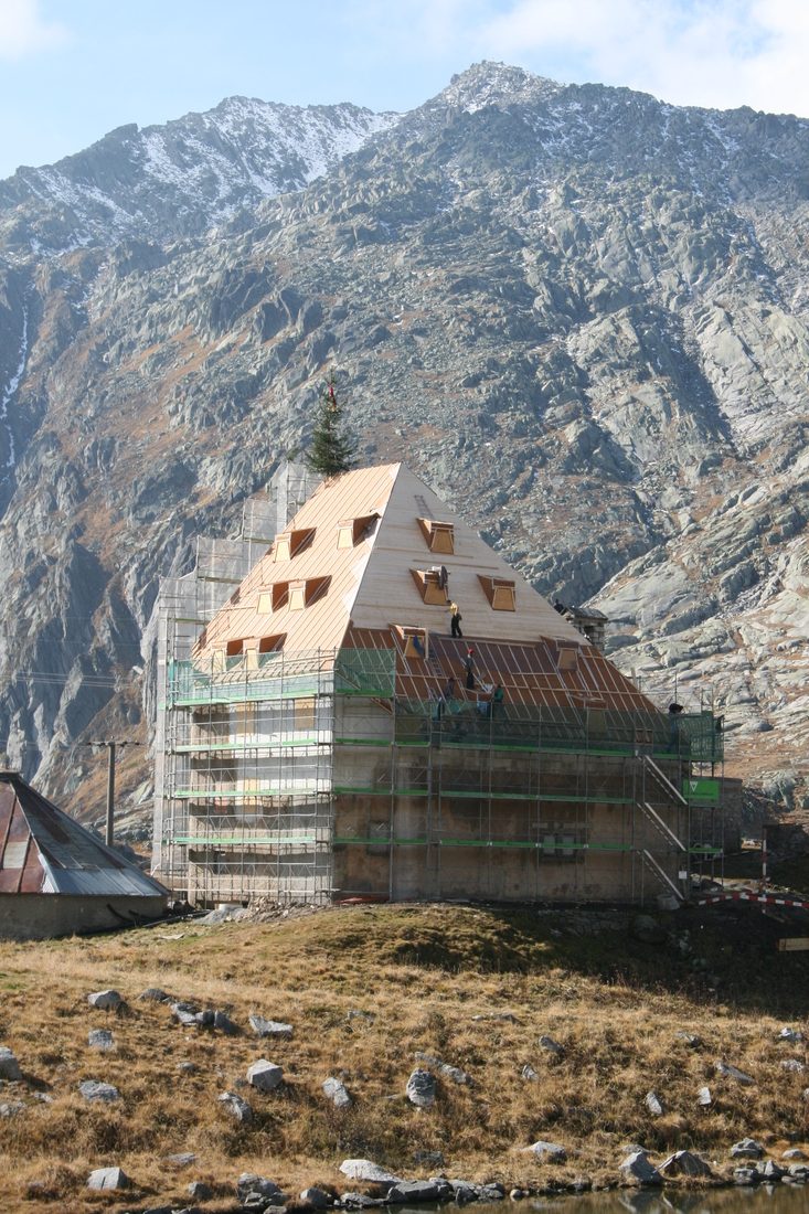Bâtiment en rénovation sur un site de montagne, avec échafaudages et toiture en cours de construction, sur fond de massif rocheux.