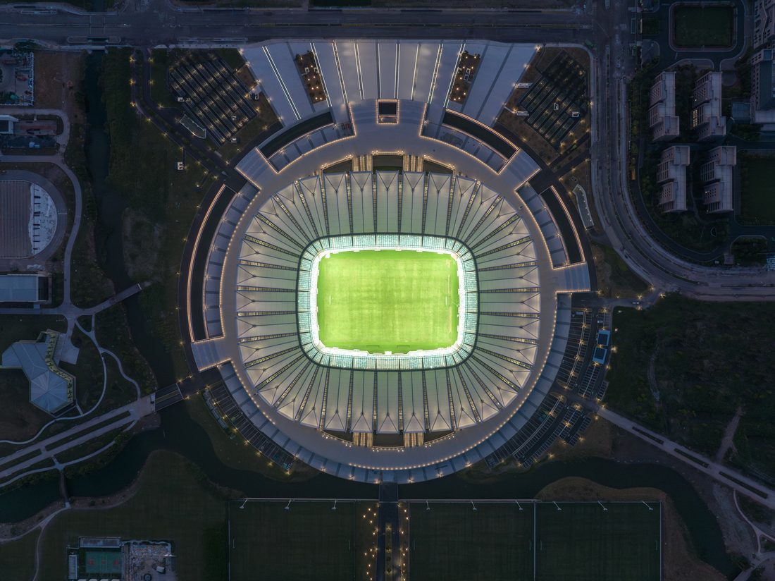 Aerial night view of Kunshan Stadium showing its illuminated roof and central field.