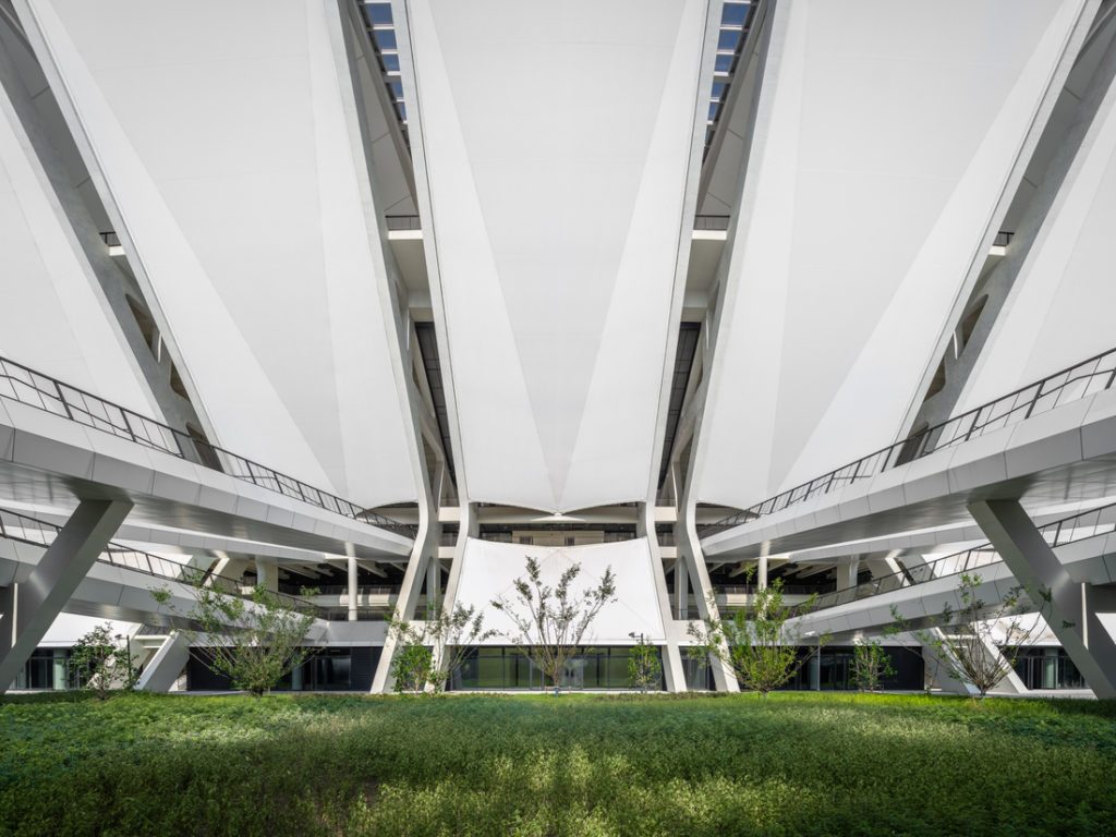 Structure architecturale moderne utilisant des membranes composites souples Serge Ferrari, avec un espace végétalisé central.