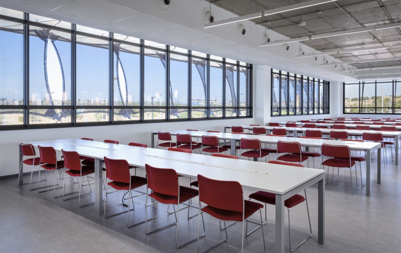 Salle de cours lumineuse avec grandes baies vitrées et chaises rouges