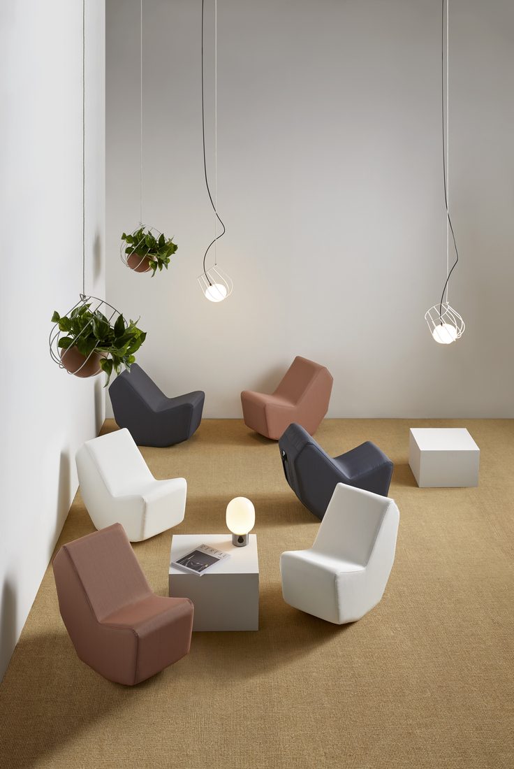 Fauteuils lounge aux formes arrondies disposés en cercle dans un intérieur minimaliste avec suspensions et plantes suspendues.