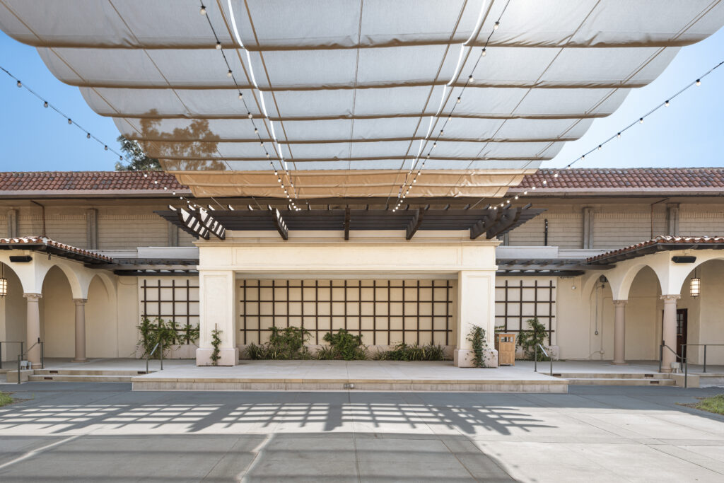 Centered view of the pavilion wall and trellis backdrop beneath the shade canopy, with arcades on both sides.