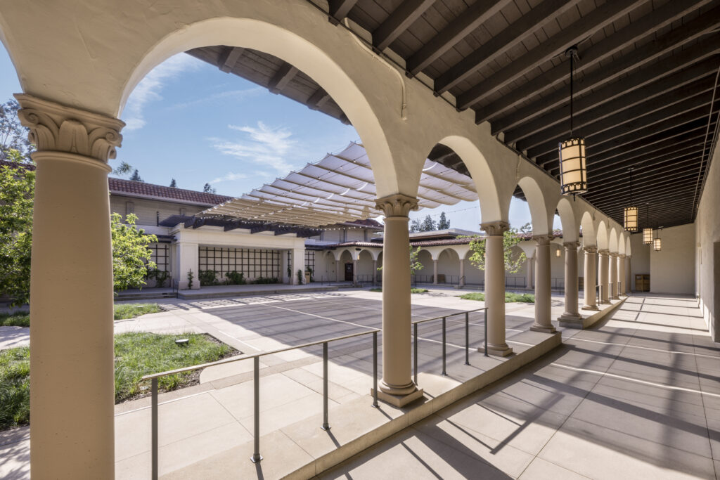 Daytime view along the arched colonnade with lanterns, looking toward the courtyard and canopy shadows.