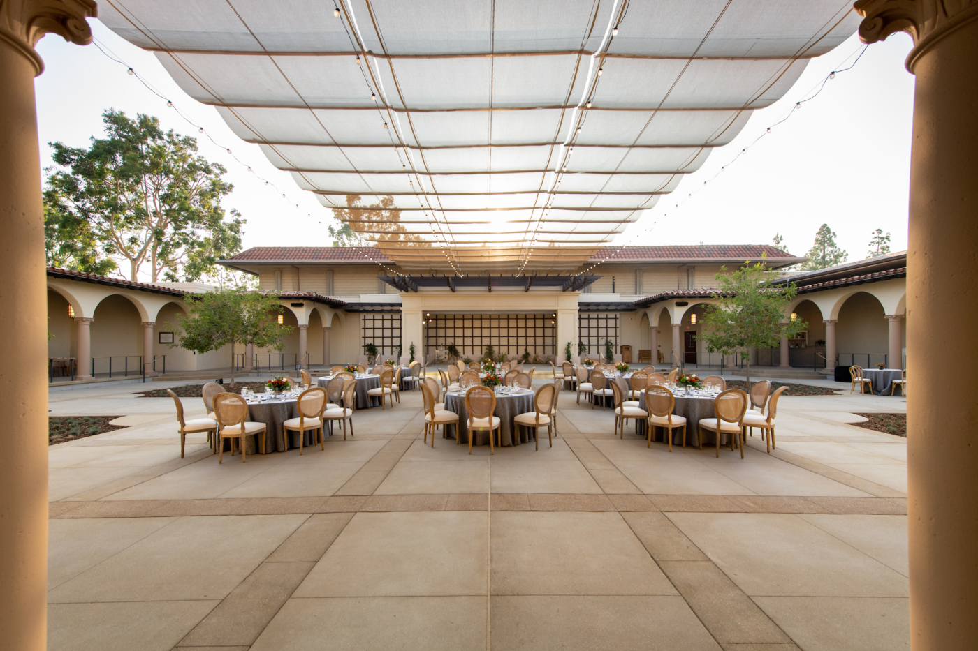 Round tables set for an event under a stretched shade canopy in Cannon Plaza, surrounded by arched walkways.