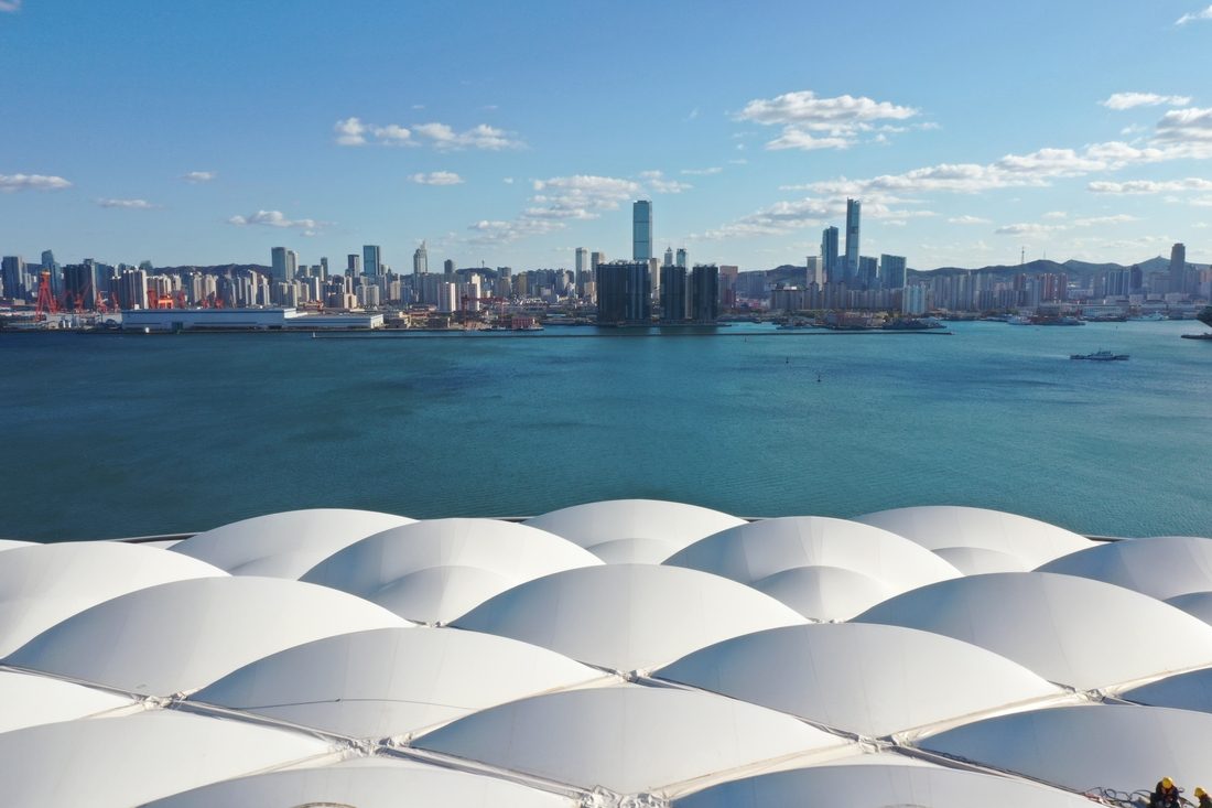 Détail de la toiture PTFE du stade de Dalian avec vue sur la skyline en bord de mer.