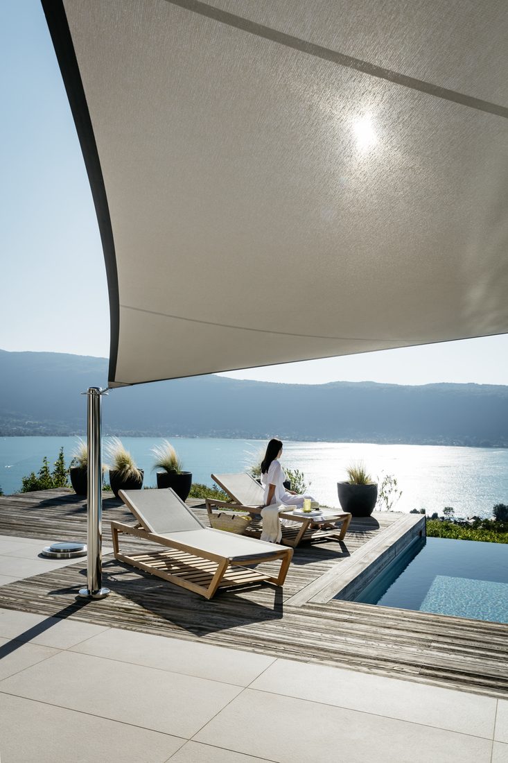 Voile d’ombrage tendu gris clair au-dessus d’une piscine, avec vue sur la mer