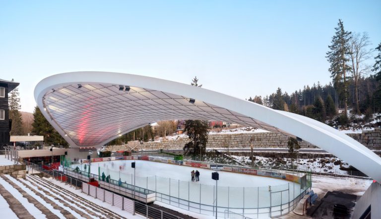 Curved tensile canopy covering the Schierker Feuerstein Arena ice rink in winter conditions