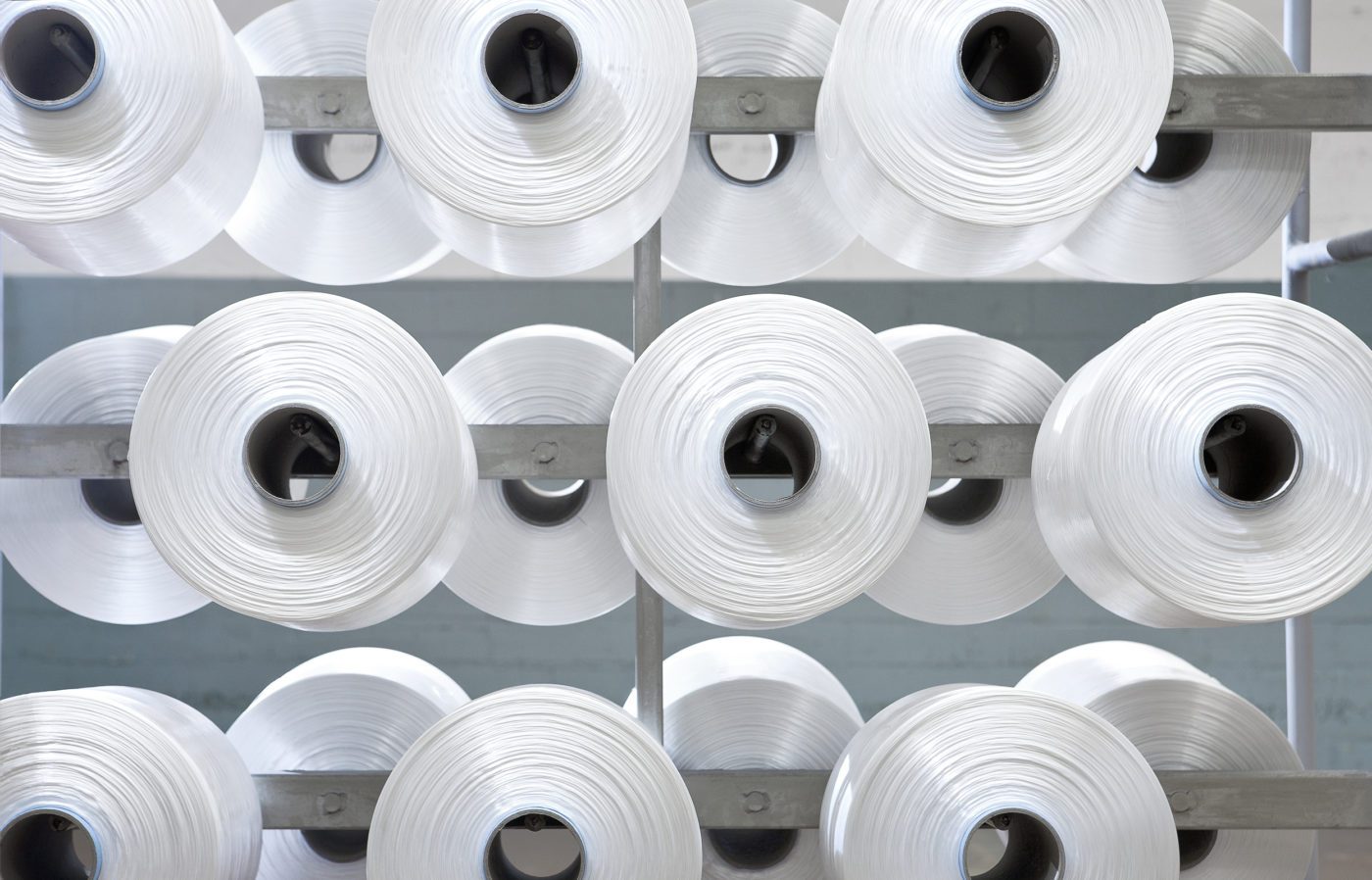 Entrepôt suisse de Serge Ferrari Tersuisse — rangée de bobines de fils industriels prêts pour la production.