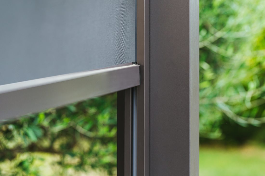 Détail de store extérieur avec toile en membrane composite souple Serge Ferrari et système de guidage latéral pour une protection solaire durable.