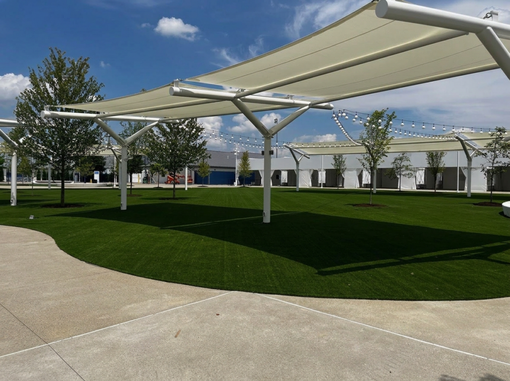White shade sails over green lawn with trees and outdoor lighting in a landscaped space.
