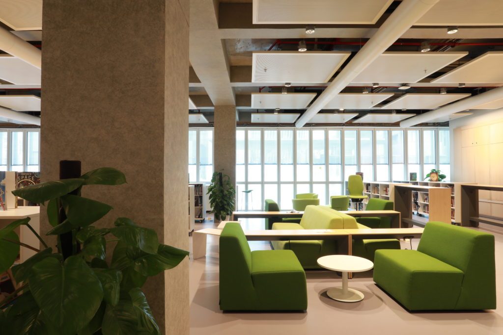 Espace intérieur contemporain et lumineux, aménagé avec des assises vertes et des tables basses, dans un environnement ouvert type école ou espace de travail.