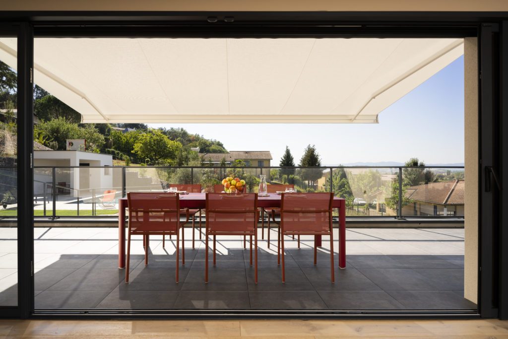 Terrasse ombragée par un store banne en membrane composite souple Soltis Serge Ferrari pour confort extérieur